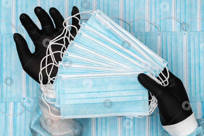 Скачать Врач держит в руках много синих хирургических медицинских масок для лица в черных защитных перчатках фотосток Ozero