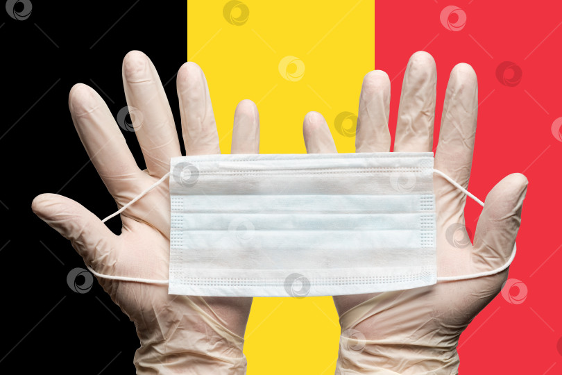 Скачать Врач держит медицинскую маску для лица двумя руками в белых перчатках на фоне флага Бельгии фотосток Ozero