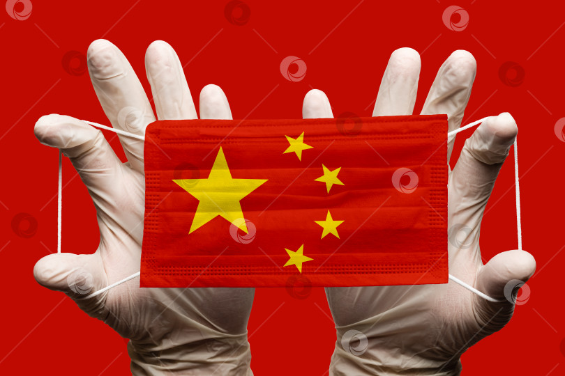 Скачать Врач держит в перчатках защитную медицинскую маску для лица, респираторную повязку с наложенным на маску национальным флагом Китая. Концепция на красном фоне фотосток Ozero