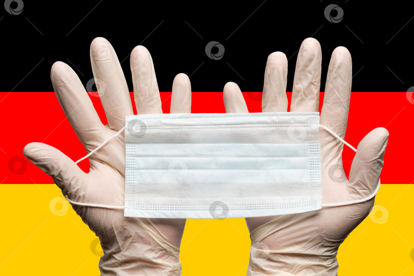 Скачать Врач держит медицинскую маску для лица двумя руками в белых перчатках на фоне флага Германии фотосток Ozero