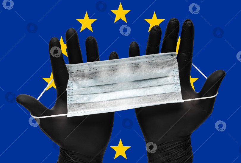 Скачать Врач держит в руках маску для лица в черных медицинских перчатках на фоне цветов флага Европейского союза EU. Страхование от пандемии коронавируса фотосток Ozero