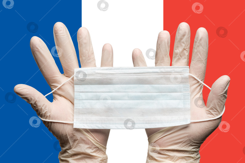 Скачать Фельдшер держит медицинскую маску двумя руками в белых перчатках на фоне флага Франции фотосток Ozero