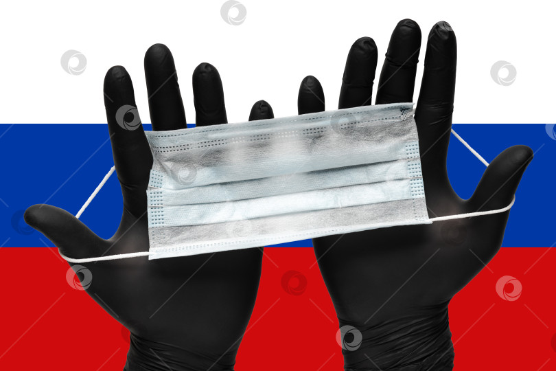 Скачать Врач держит в руках маску для лица в черных медицинских перчатках на фоне цветов флага России или российского флагштока. Страхование от пандемии коронавируса фотосток Ozero