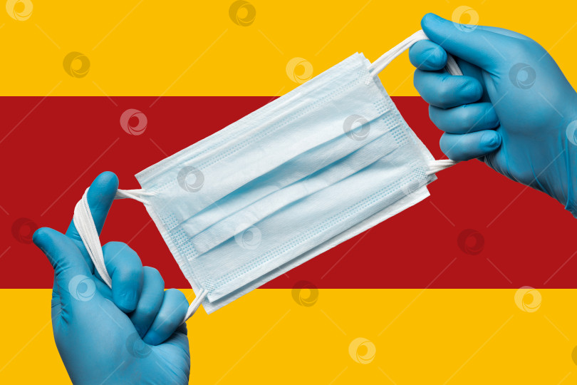 Скачать Медик в синих перчатках держит респираторную маску в руках на фоне флага Испании. Концепция карантина по коронавирусу, вспышка пандемии фотосток Ozero