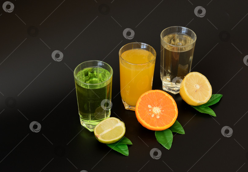 Скачать Три бокала с разными цитрусовыми соками на черном фоне, рядом со спелыми фруктами. фотосток Ozero