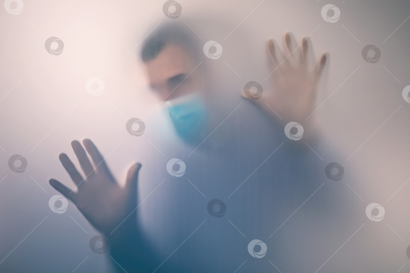 Скачать Человек в медицинской маске за матовым стеклом. Концепция на тему карантина в больнице. Расфокусированный фон фотосток Ozero