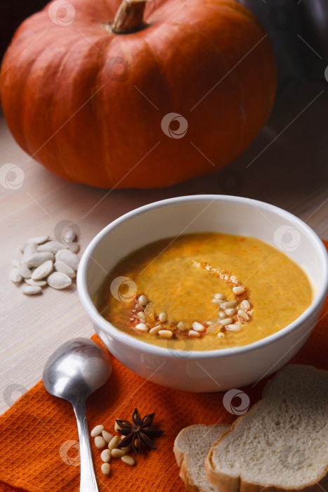 Скачать Домашний тыквенный суп со свежей тыквой и ярко-оранжевой кухонной скатертью на белом столе фотосток Ozero