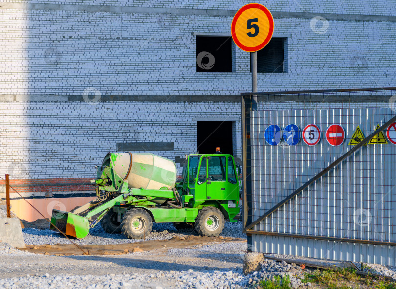 Скачать Небольшая автомобильная бетономешалка возле строящегося здания на строительной площадке. Зеленый бетоновоз. фотосток Ozero