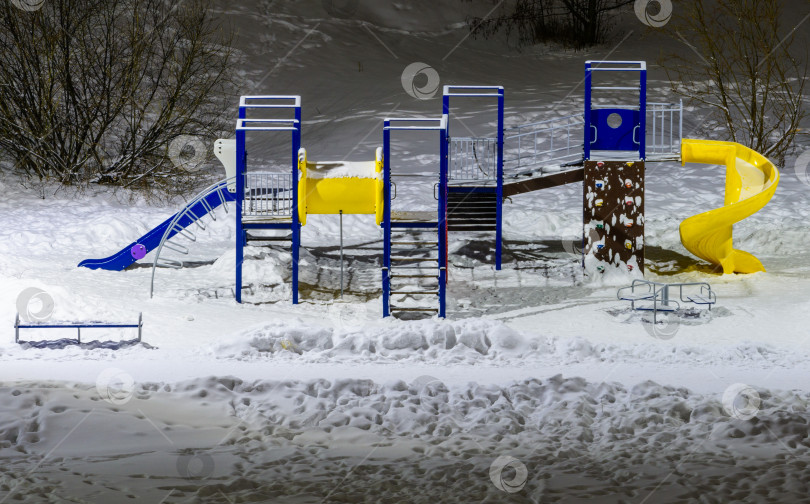 Скачать Вид сверху на освещенную игровую площадку во дворе в городе зимой. Концепция строительства детских игровых площадок с ночным освещением. фотосток Ozero