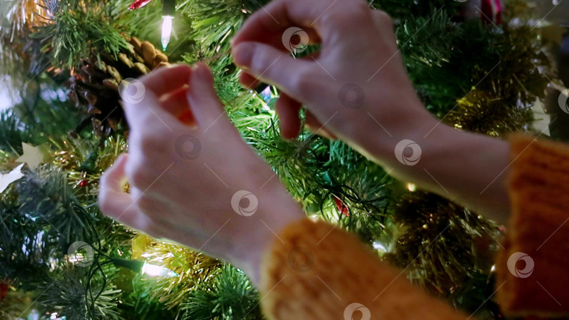 Скачать Крупный план женских рук в желтом кардигане, украшающих рождественскую елку винтажным серебряным шаром. Подготовка к праздникам фотосток Ozero