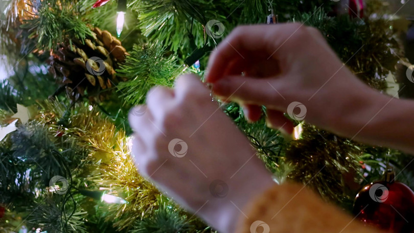 Скачать Женские руки украшают елку игрушками. Подготовка к праздникам. Крупный план фотосток Ozero