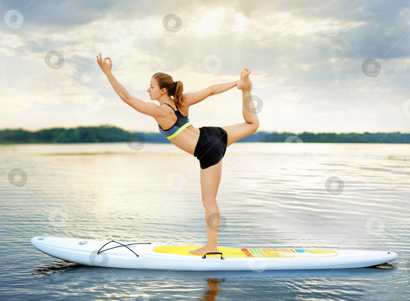 Скачать Женщина, практикующая позу йоги "Повелитель танца", балансирующая на доске для гребли фотосток Ozero