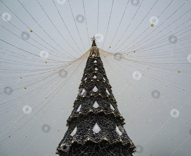 Скачать Заснеженная рождественская елка с гирляндами и украшениями. Новогодние светящиеся гирлянды расходятся с верхушки ели в разные стороны. фотосток Ozero