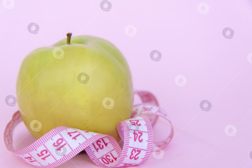 Скачать Зеленое яблоко и сантиметровая рулетка на розовом фоне. Спорт, спортивное питание, здоровое питание, диета. Пробел для текста. фотосток Ozero