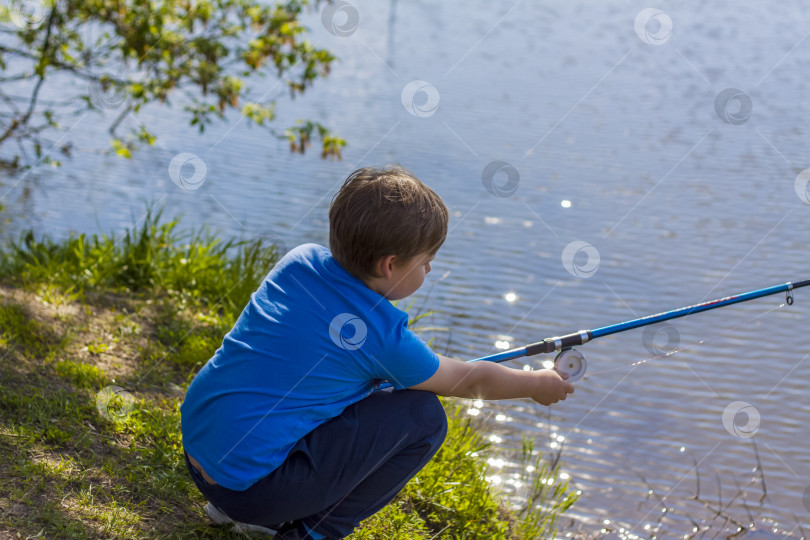 Скачать Мальчик сидит на берегу озера с удочкой и ловит рыбу. Маленький рыбак. Ребенок ловит рыбу в реке. фотосток Ozero