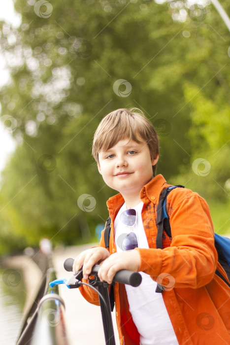 Скачать Ребенок-подросток мчится на самокате по парку. Молодой человек в парке в солнечную погоду. фотосток Ozero