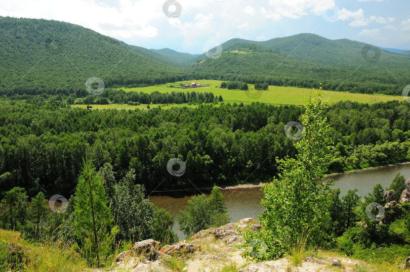 Скачать Вид через широкую реку и лес на большую ферму на склоне высокой горы, окруженную хвойным лесом. фотосток Ozero