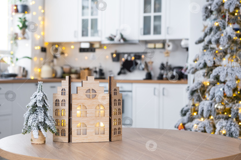 Скачать Уютный рождественский декор крошечного домика небольшого размера на столе праздничной белой современной кухни. Подарок на Новый год. Страхование, переезд в новый дом, ипотека, аренда и покупка недвижимости фотосток Ozero