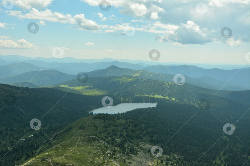 Скачать Вид на узкую тропинку с вершины, спускающуюся по склону к озеру в живописной горной долине под облачным летним небом. фотосток Ozero