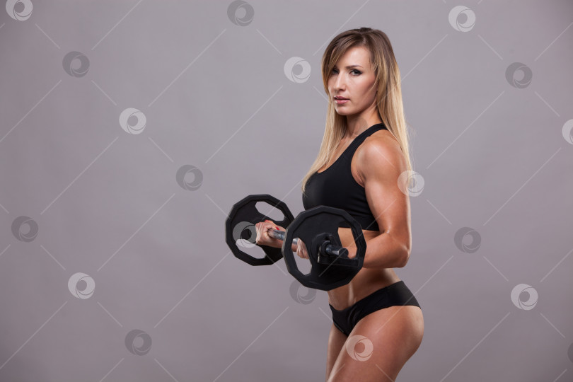 Скачать Красивая спортивная женщина в спортивной одежде качает мышцы со штангой, выделенной на сером фоне с помощью copyspace фотосток Ozero