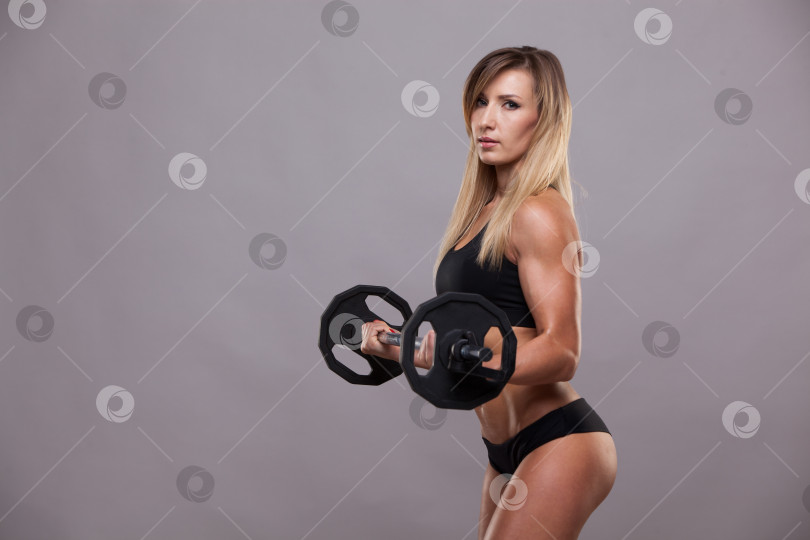 Скачать Красивая спортивная женщина в спортивной одежде качает мышцы со штангой, выделенной на сером фоне с помощью copyspace фотосток Ozero