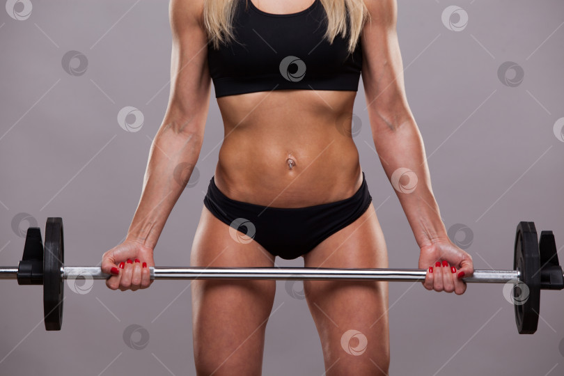 Скачать Крупным планом атлетический торс женщины в спортивной одежде. Она держит штангу на сером фоне с copyspace фотосток Ozero