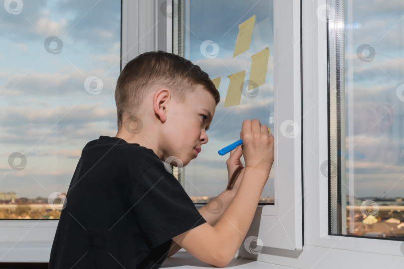 Скачать Маленький мальчик пишет на наклейке, приклеенной к окну фотосток Ozero