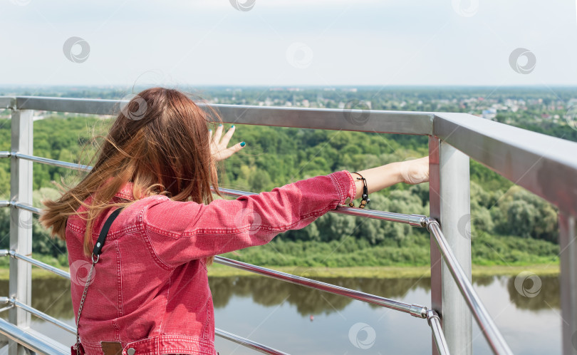Скачать Молодая девушка смотрит на город с панорамного балкона фотосток Ozero