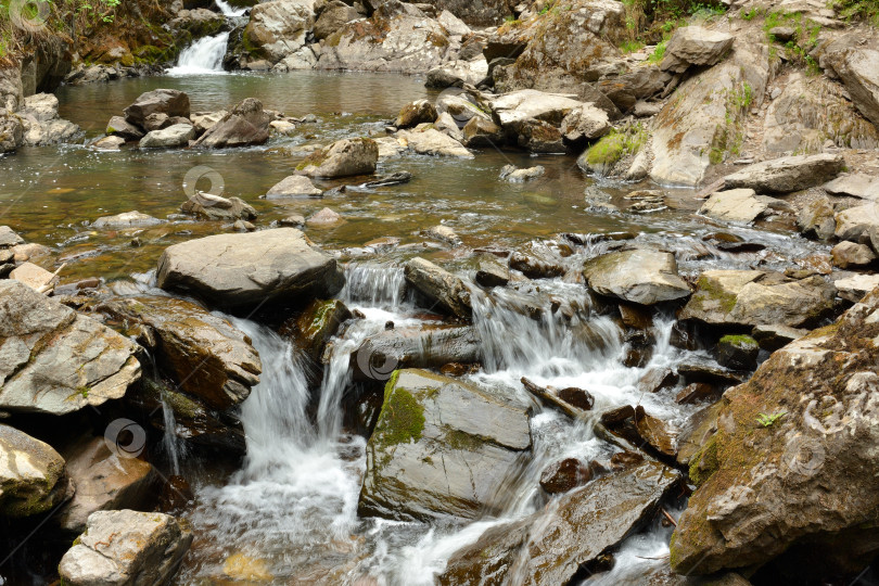 Скачать Небольшая речка в скалистых берегах низвергается каскадом с гор через утренний лес после дождя. фотосток Ozero
