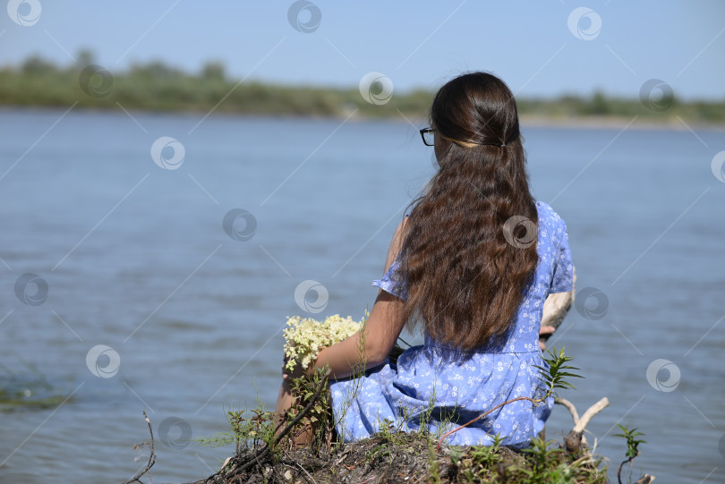 Скачать Молодая девушка с длинными темными волосами стоит на берегу реки. фотосток Ozero