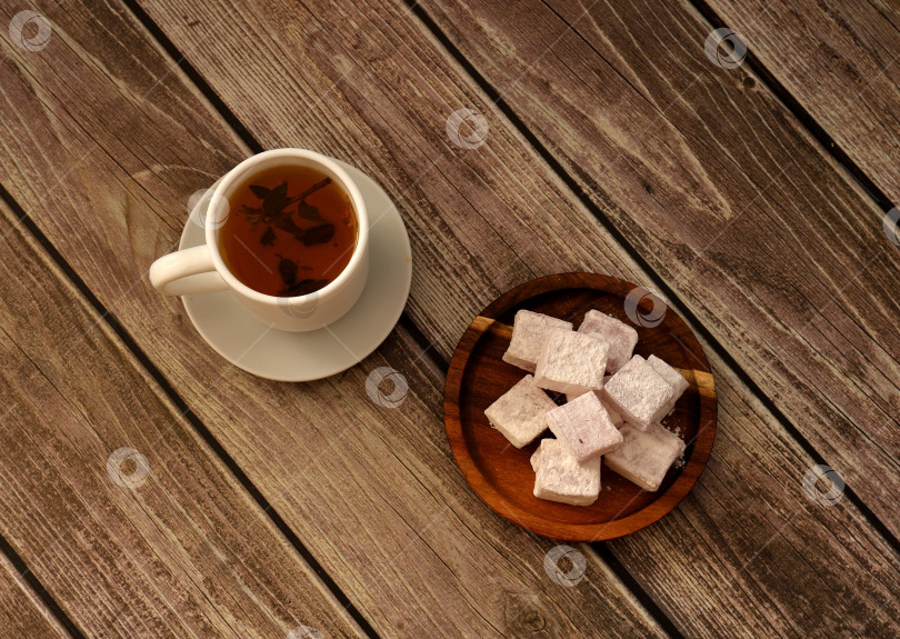 Скачать Чашка горячего чая на блюдце с круглой деревянной тарелкой с кучей восточных сладостей в сахарной пудре на деревянном столе. фотосток Ozero