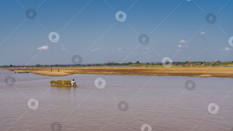 Скачать Каноэ, груженное сеном, плывет по спокойной красно-коричневой воде. фотосток Ozero