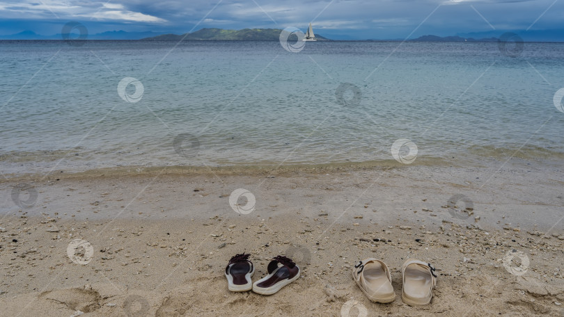 Скачать На песчаном пляже, у кромки воды, стоят две пары шлепанцев фотосток Ozero