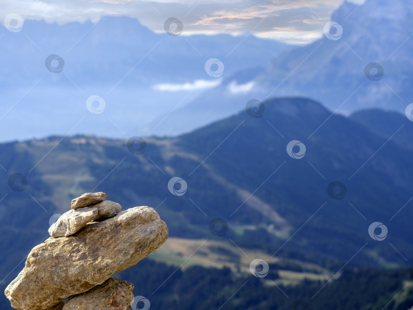 Скачать Груда камней, сложенных друг на друга на краю обрыва. На заднем плане видны горные хребты. Естественный горный пейзаж с пирамидой из камней крупным планом. фотосток Ozero
