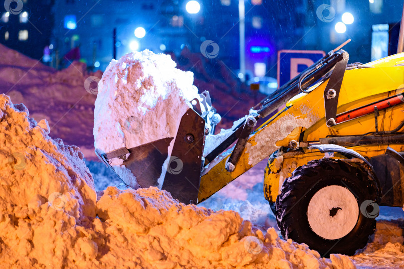 Скачать Снегоуборочная машина, трактор убирают снег на проезжей части улицы в снежную бурю ночью. Служба уборки снега, работающая зимой. фотосток Ozero