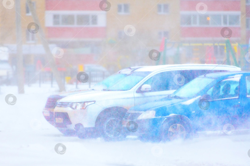 Скачать Череповец, Россия, 27 ноября 2023 года, автомобили припаркованы на заснеженной парковке на городской улице во время сильного снегопада зимой.  Прогноз погоды на дорогах в метель.Плохая видимость. фотосток Ozero