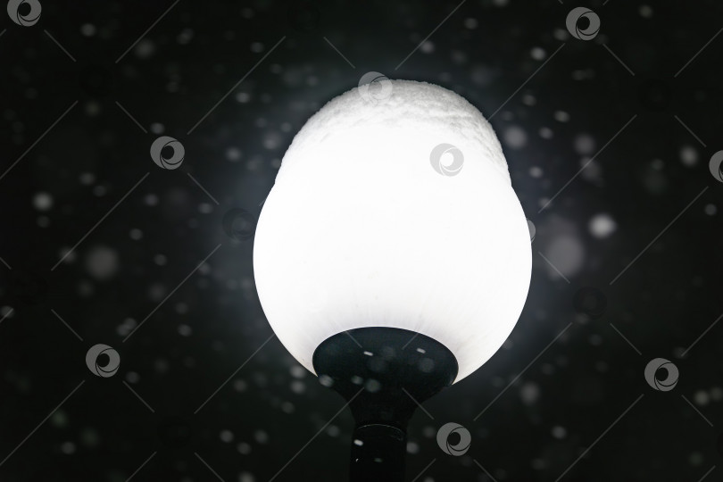 Скачать Уличный фонарь в селективном фокусе светит во время снегопада, метели, шторма зимней ночью. фотосток Ozero