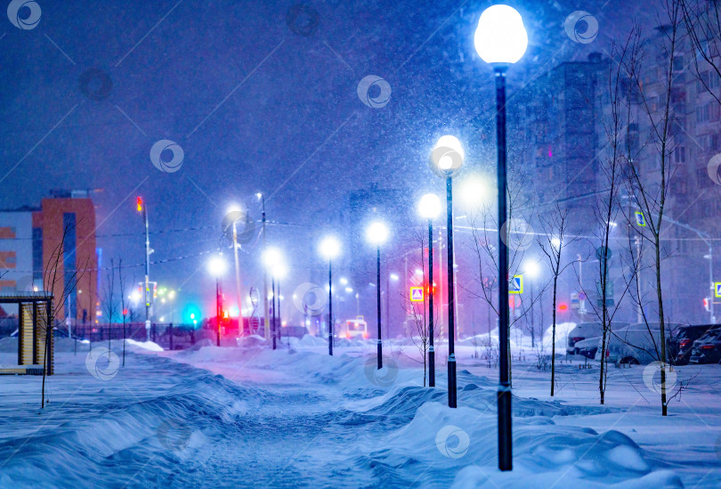 Скачать Фонарный столб в выборочном фокусе во время снежной бури освещает аллею зимним вечером.Уличные фонари в городе создают рождественское настроение на прогулке. фотосток Ozero