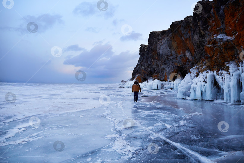 Скачать Замерзшее озеро Байкал на закате. Мужчина-путешественник прогуливается по прозрачному льду озера. фотосток Ozero