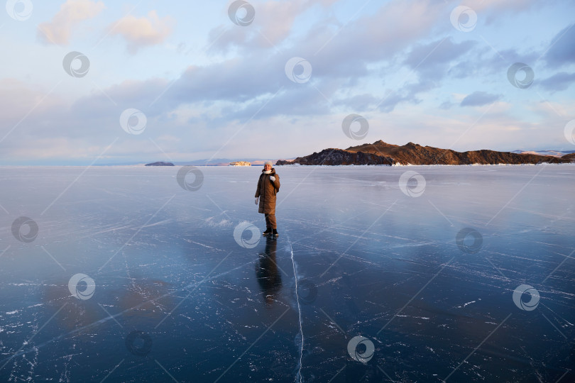 Скачать Прекрасный пейзаж замерзшего озера Байкал на закате. Молодая женщина прогуливается по прозрачному льду озера. фотосток Ozero