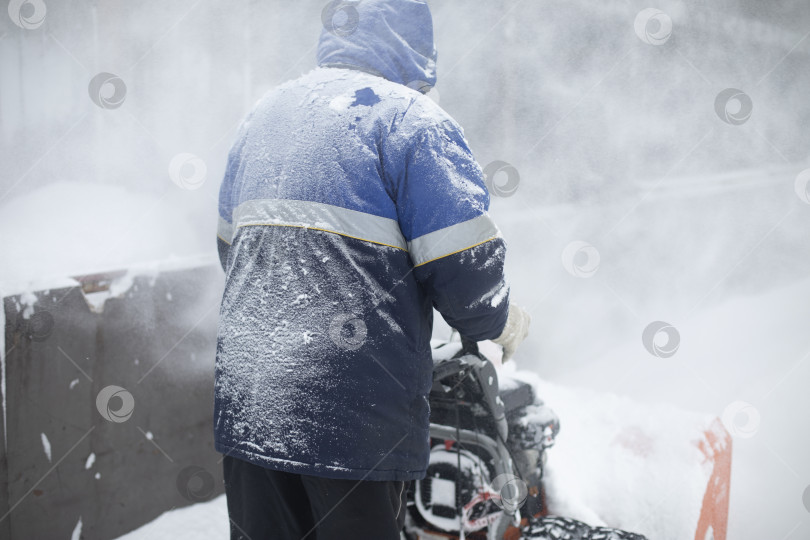 Скачать Мужчина убирает снег. Снегоуборочная техника на улице. Машина для откидывания снега со льда. фотосток Ozero