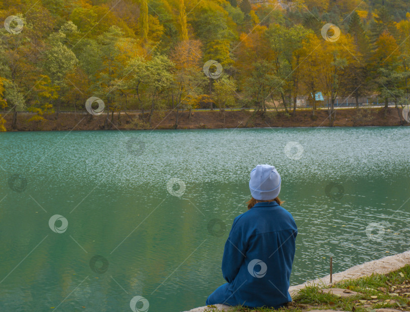 Скачать Одинокая женщина сидит на берегу горного лесного озера. Осенний пейзаж, тишина, умиротворение, путешествия. фотосток Ozero