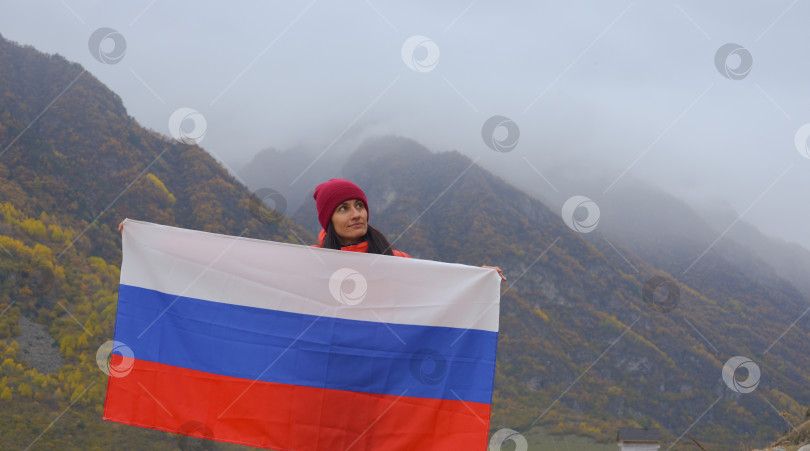 Скачать Крупный план российского флага, красиво развевающегося в руках женщины на фоне Кавказских гор в пасмурный туманный день. День независимости России фотосток Ozero