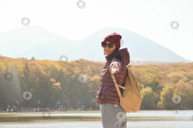 Скачать Красивая женщина с рюкзаком за спиной улыбается в камеру и отдыхает на пирсе озера в горах. Концепция отдыха фотосток Ozero