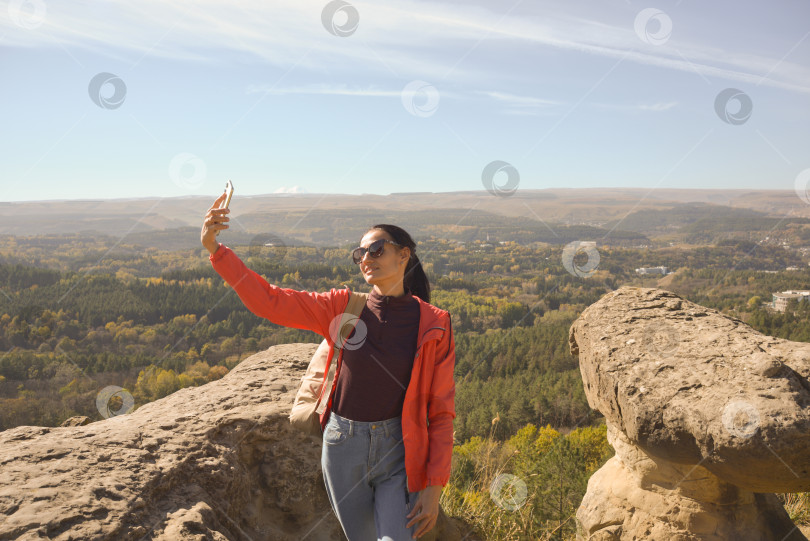 Скачать Молодая красивая женщина-путешественница, делающая селфи-портрет на вершине горы - Счастливая улыбающаяся девушка с помощью смартфона - Пеший туризм и скалолазание фотосток Ozero