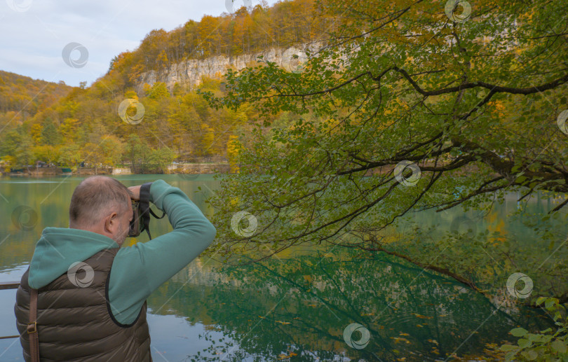 Скачать Турист-мужчина фотографирует красивый осенний пейзаж с озером в горах фотосток Ozero