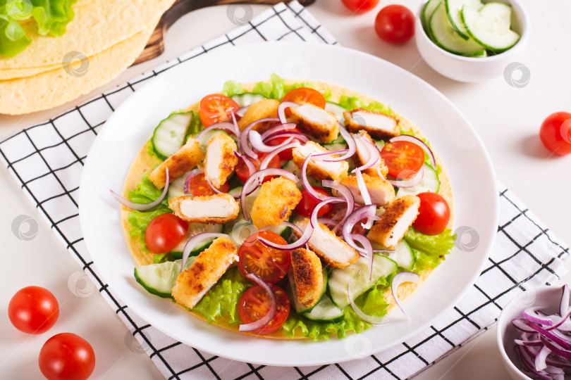 Скачать Тортилья с наггетсами, овощами и листьями салата на тарелке на столе фотосток Ozero
