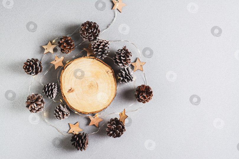 Скачать Рождественский фон, гирлянда и сосновые шишки вокруг срезанного ствола дерева на сером фоне фотосток Ozero