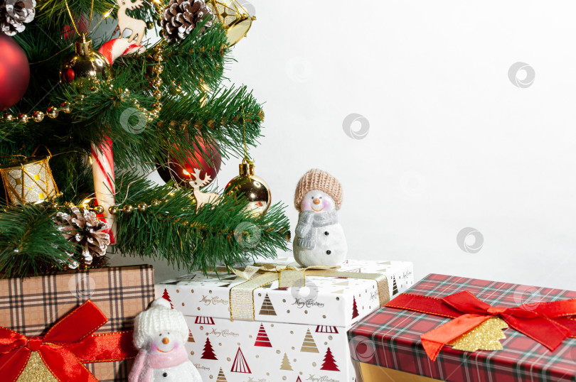 Скачать Рождественская елка с игрушками и деревянной гирляндой на белом фоне. Подарочная коробка с крышкой в шотландскую клетку под искусственно украшенной рождественской елкой. Макет. Nouvelle annee. Ноэль фотосток Ozero