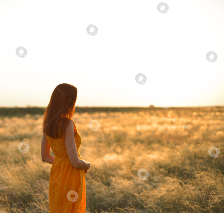 Скачать Симпатичная молодая девушка с длинными каштановыми волосами в оранжевом платье в поле на закате. Концепция свободы и природы. фотосток Ozero